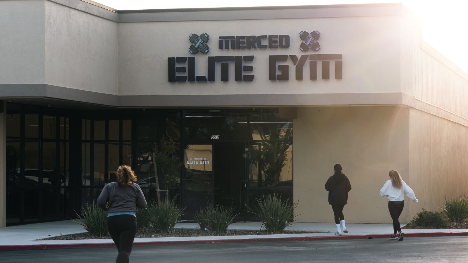 The exterior of Merced Elite Gym at 659 in Merced, California, with women walking in through the front entrance at sunrise